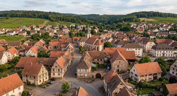 Photographie aérienne ou vue panoramique de la commune de Mutzig en Alsace (Bas-Rhin), montrant un environnement résidentiel typique avec habitations, toitures, rues et espaces périurbains. L'image doit transmettre un sentiment de proximité locale et représenter une petite commune alsacienne où intervient l'entreprise de rénovation, visuellement distincte d'une vue similaire de Fegersheim.